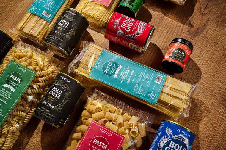 Alle vier Bolognese-Sorten mit Pasta-Packungen auf einem Holztisch