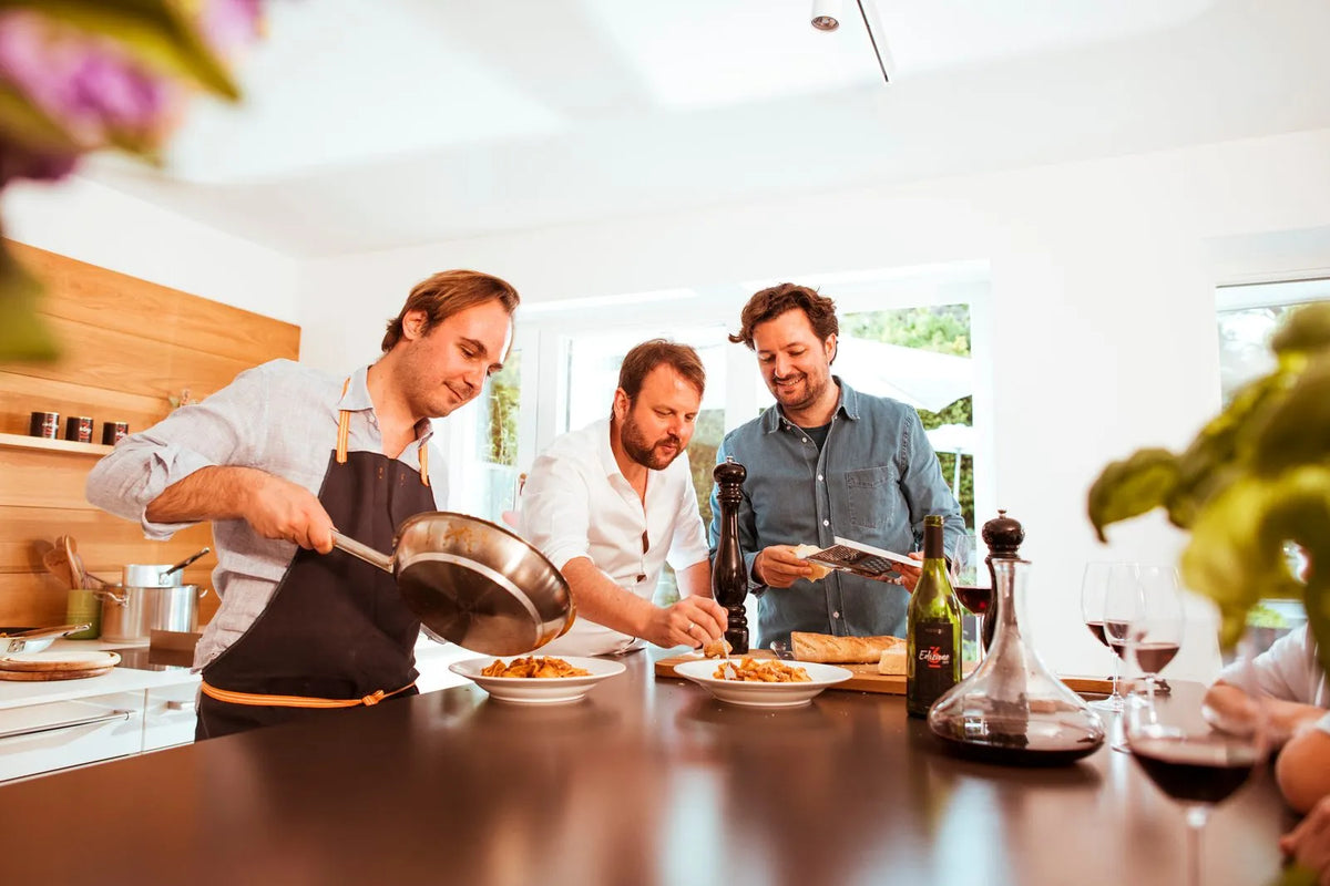 Drei Freunde kochen gemeinsam Pasta, auf dem Tisch Rotwein
